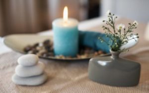 lit candle on a table next to a flower and a small stack of rocks